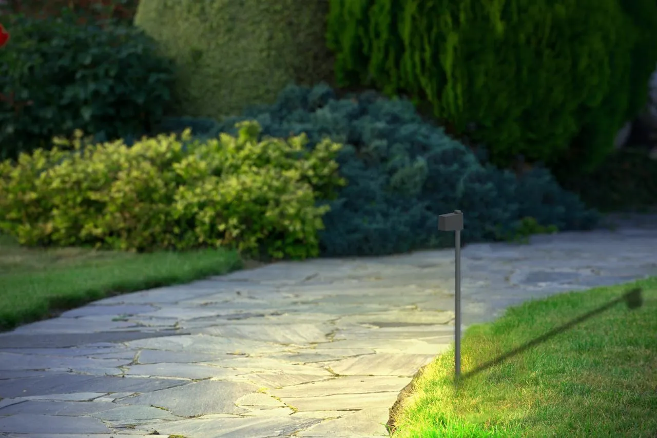 Slim pole path light with a compact rectangular head, lighting a garden walkway